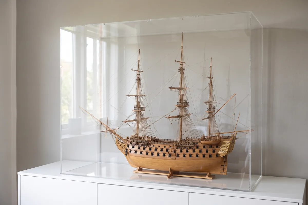 Historic sailing ship model with full rigging under a tall acrylic display case