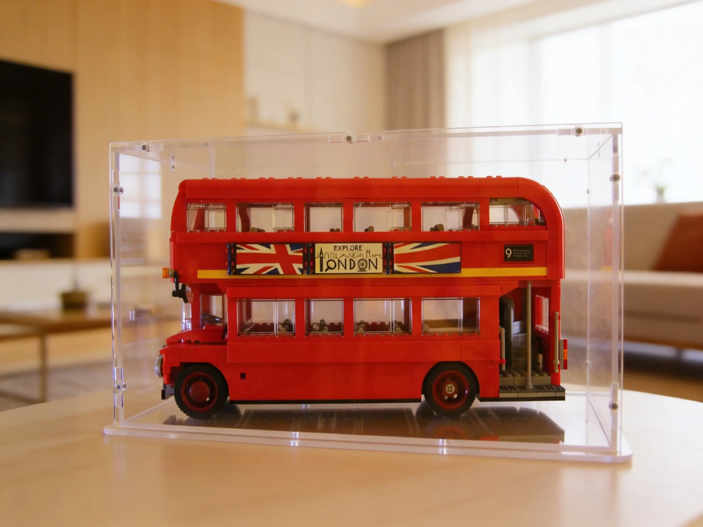 Sora acrylic display case over a LEGO Creator London double-decker bus with a Union Jack advertising board on a wooden table